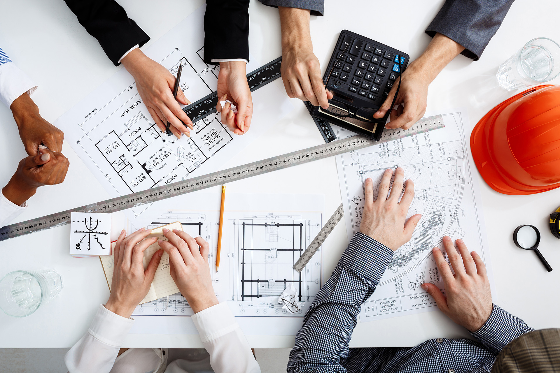 A Team of Chartered Surveyors Sitting Around Blueprints and Stationery Discussing Project Management Design Alterations Plans