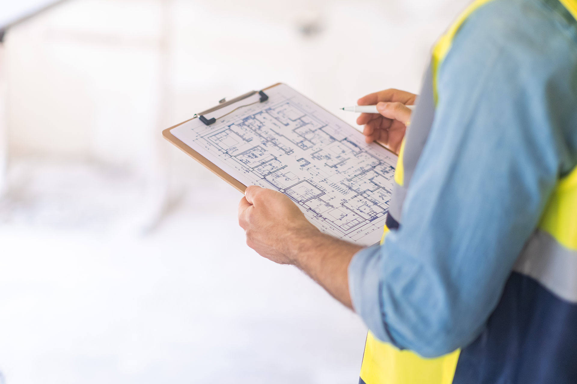 A Building Surveyor In A Hi-Viz Vest Holding Clipboard With RICS Home Survey Documents